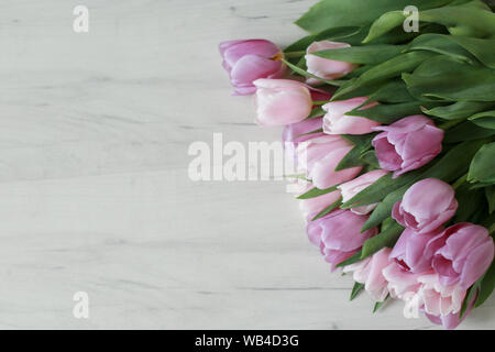Bicchieri, tulipani e accessori in colore rosa su bianco tavolo in legno Foto Stock