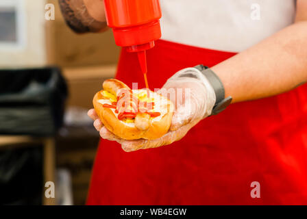 Le mani di chef di strada aggiungendo il ketchup su hot dog close up Foto Stock