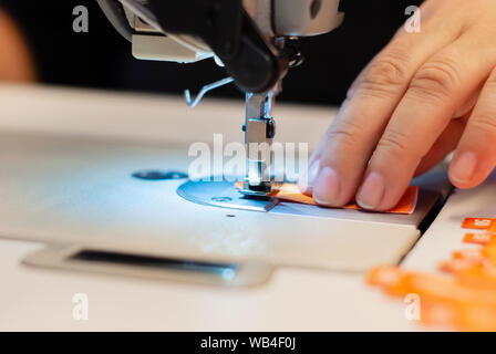 Mano sarta e il piedino della macchina per cucire overcasting mentre i bordi della etichetta di tessuto di close-up Foto Stock