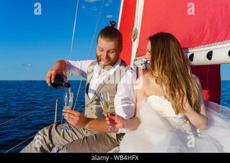 Speciale sposi in viaggio di nozze al mare su una barca a vela, versando il vino spumante Foto Stock