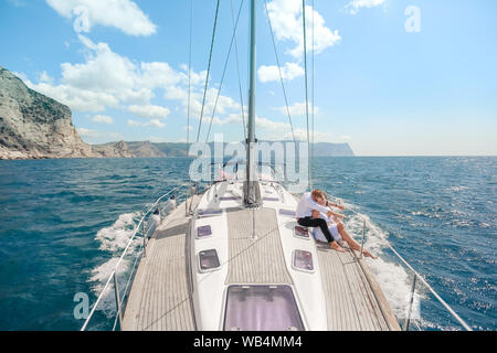 Bianco con yacht a vela va impostata lungo l'isola in una giornata calda. Il mare blu, blu cielo. La Crimea. a bordo di una giovane coppia in amore. la sposa e lo sposo. weddin Foto Stock