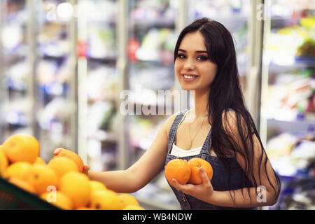 Un cliente in un centro commerciale sceglie le arance. La ragazza nel negozio di frutta tiene nelle sue mani Foto Stock