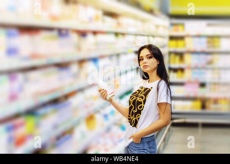 Giovane bella ragazza può contenere una bottiglia di latte nelle sue mani sullo sfondo di una scaffalatura con il cibo in un centro commerciale Foto Stock