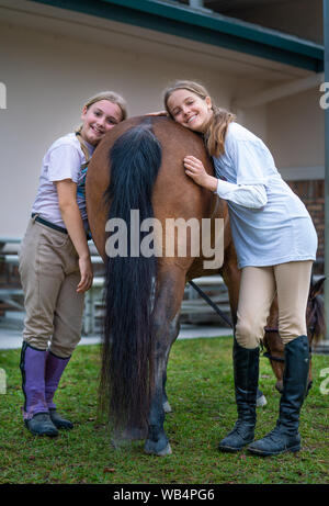 Due ragazze equestre sono in piedi accanto al cavallo la schiena e sorridendo alla telecamera a uno spettacolo di cavalli Foto Stock