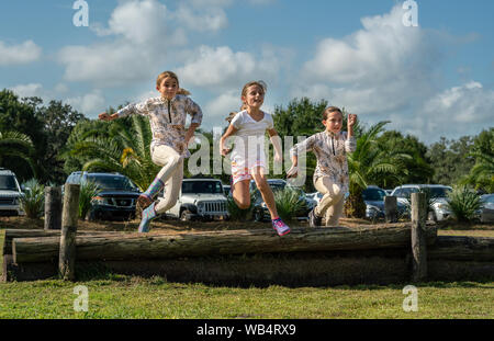 Tre giovani ragazze caucasiche sono saltando su un registro insieme ad uno spettacolo di cavalli durante l'attesa per i loro compagni di squadra per competere Foto Stock