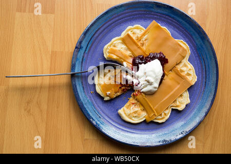 Formaggio norvegese marrone su un waffle con marmellata di fragole e panna acida parzialmente mangiato con una forchetta Foto Stock