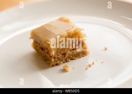 Pezzo unico di quadrato di butterscotch su piatto bianco con briciole Foto Stock