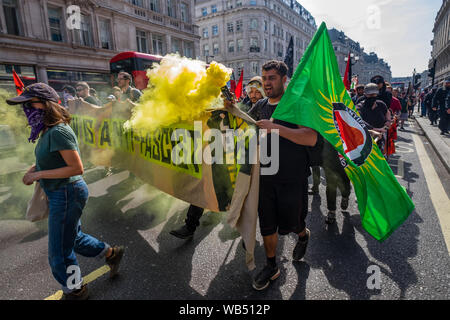 Londra, Regno Unito. 24 agosto 2019. Anti-fascisti luce una svasatura di fumo come essi marzo per opporsi a una protesta presso la BBC da Tommy Robinson sostenitori che affermano che egli è in carcere per il giornalismo. Egli è stato condannato a 9 mesi per 3 reati al di fuori di Leeds Crown Court che potrebbe aver causato il crollo di una toelettatura pista di prova e ha precedenti condanne per violenza, finanziari e frodi in materia di immigrazione, del possesso di droga e di ordine pubblico reati. La polizia ha mantenuto la due gruppi separati. Robinson sostenitori sono stati successivamente unite dai dimostranti da Trafalgar Square, e un gruppo di grandi dimensioni dal supporto fino al razzismo è venuto per unire Antifa Foto Stock