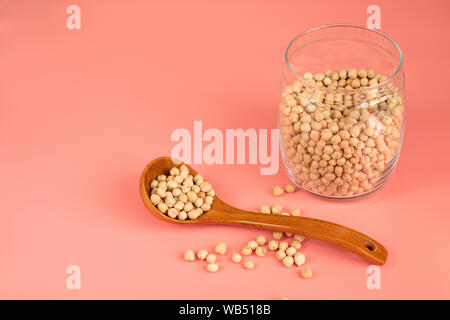 I ceci in un vaso di vetro con un cucchiaio di legno su un sfondo rosa Foto Stock