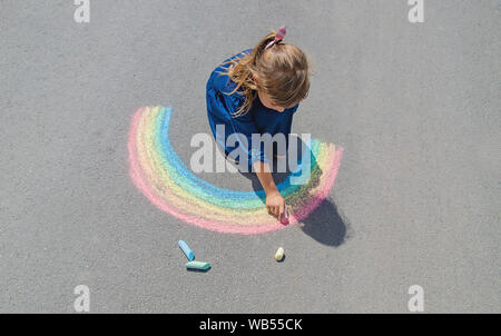 Bambino disegna con un gessetto sul marciapiede. Messa a fuoco selettiva. Foto Stock