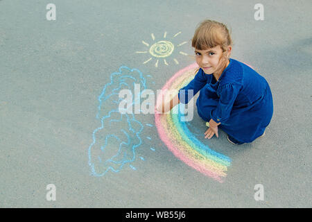 Bambino disegna con un gessetto sul marciapiede. Messa a fuoco selettiva. Foto Stock