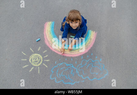 Bambino disegna con un gessetto sul marciapiede. Messa a fuoco selettiva. Foto Stock