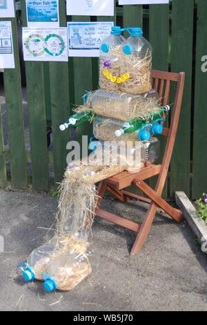 Rennington, Inghilterra, 24 agosto 2019. Uno spaventapasseri di paglia riempito di bottiglie di plastica dei rifiuti evidenziando seduto su una sedia di legno durante lo spaventapasseri festival che si tiene ogni anno a Ferragosto weekend. Foto Stock