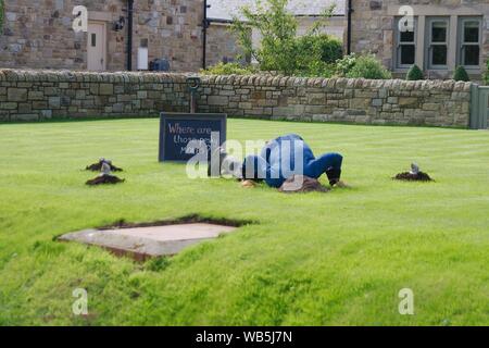 Rennington, Inghilterra, 24 agosto 2019. Uno spaventapasseri seppellisce la sua testa nel giardino alla ricerca di moli, chi sta guardando a lui dagli altri fori, durante The scarecrow festival che si tiene ogni anno a Ferragosto weekend. Foto Stock