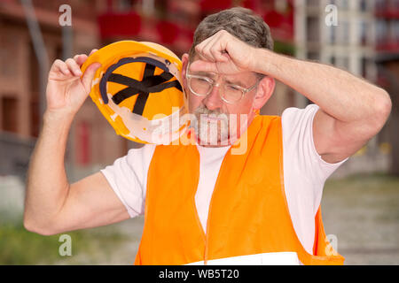 Ritratto di bello il lavoratore nel suo 50s con casco cercando stanco Foto Stock