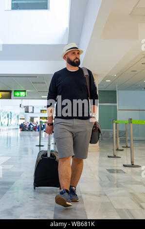 Giovane con hat passeggiando per il terminal di un aeroporto che porta una valigia Foto Stock