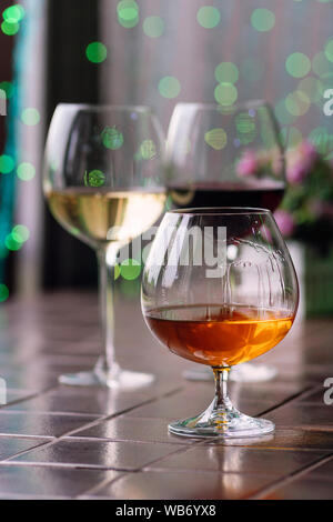 Il Brandy in tipico snifter. Cognac in elegante vetro con spazio per il testo su sfondo colorato. Due bicchieri di vino in background unfocus. Degustazione, res Foto Stock