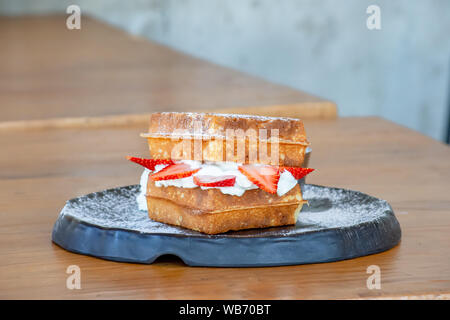 Waffle Strawerry panna fresca nella piastra nera su un tavolo di legno. Foto Stock