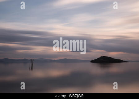 Bellissima vista del tramonto al lago Trasimeno (Umbria, Italia), con le nuvole e le isole riflessi sull'acqua. Foto Stock