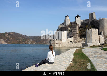 La bambina è seduta sulla sponda del fiume e sta guardando la fortezza di Golubac Serbia Foto Stock