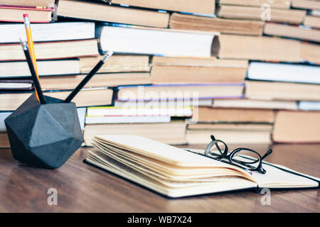 Pila di vecchio libro, penne e matite a titolare, aprire il notebook e bicchieri. Il concetto di istruzione sfondo, molti libri di pile con copia spazio per il testo Foto Stock