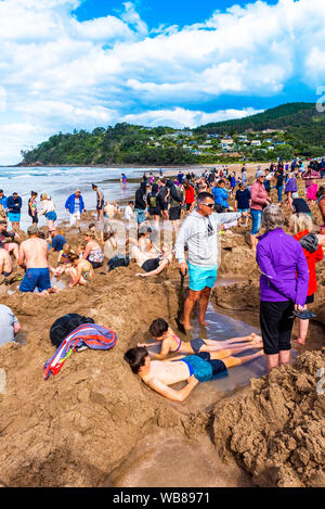 COROMANDEL, Nuova Zelanda - 13 ottobre 2018: turisti scavare buchi nella sabbia vulcanica sulla spiaggia dell' acqua calda. In verticale Foto Stock