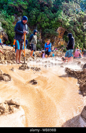 COROMANDEL, Nuova Zelanda - 13 ottobre 2018: turisti scavare buchi nella sabbia vulcanica sulla spiaggia dell' acqua calda. In verticale Foto Stock