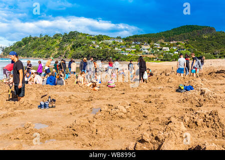 COROMANDEL, Nuova Zelanda - 13 ottobre 2018: turisti scavare buchi nella sabbia vulcanica sulla spiaggia dell' acqua calda Foto Stock