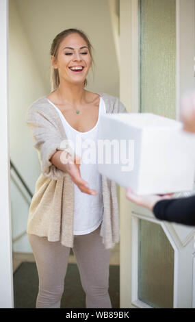 donna che riceve confezione da postino di fronte a casa, verticale Foto Stock