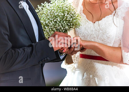 Sposi anelli di exchange, lo sposo mette l'anello sulla sposa la mano nel matrimonio ufficio del registro di sistema Foto Stock