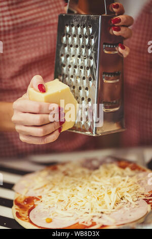 Close-up di un giovane le mani delle donne grattugiare il formaggio e metterlo sulla pizza. Foto Stock