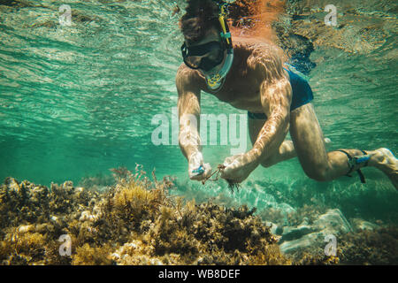 Uomo bello divertirsi in vacanza estiva ed esplorare il fondale durante le immersioni subacquee in mare. Foto Stock