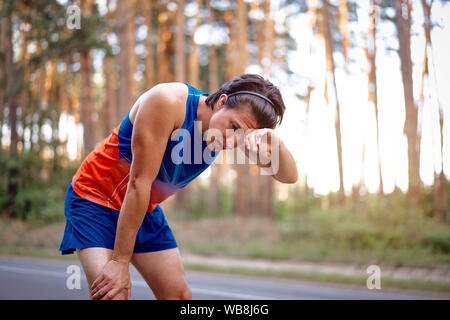 Runner uomo riposo dopo la formazione in esecuzione per il triathlon. Maschio modello fitness triatleta e rilassante. Jogging uomo prendendo una pausa durante il training outdoo Foto Stock