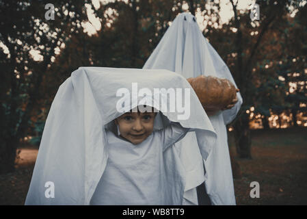 Padre e figlio la riproduzione di fantasmi con fogli bianchi nel giardino, concettuale foto per halloween vacanze Foto Stock