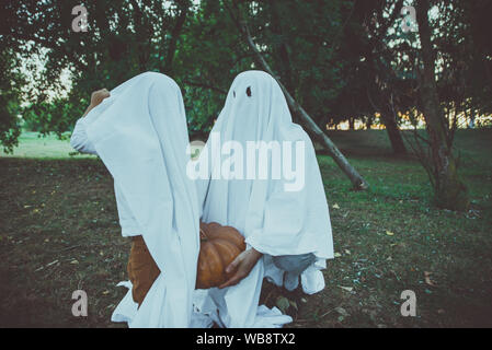 Padre e figlio la riproduzione di fantasmi con fogli bianchi nel giardino, concettuale foto per halloween vacanze Foto Stock