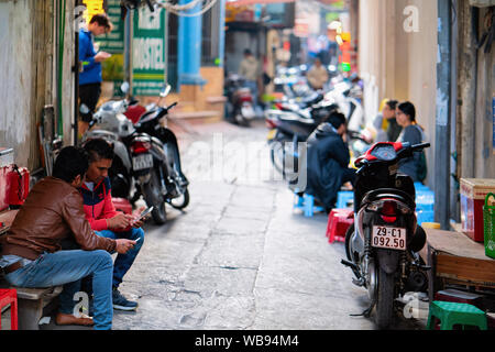 Hanoi, Vietnam - Febbraio 21, 2016: la popolazione locale e ciclomotori in strada della città di Hanoi in Vietnam nel sud-est asiatico. Gli uomini e le donne sedute, moto parcheggiate all angolo della strada. Le persone e le motociclette. Foto Stock
