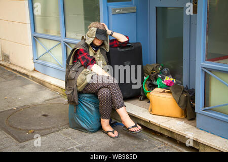 Parigi, Francia - luglio 7, 2018: donna senzatetto con sacchi e una valigia su un marciapiede in strada a Parigi Foto Stock