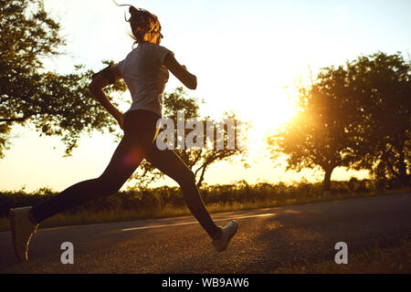 Ragazza runner corre sulla strada del sole all'alba. Foto Stock