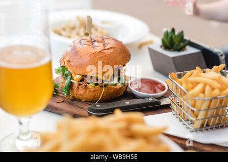 Un primo piano selettivo di patatine fritte, ketchup e hamburger su una tavola di legno Foto Stock
