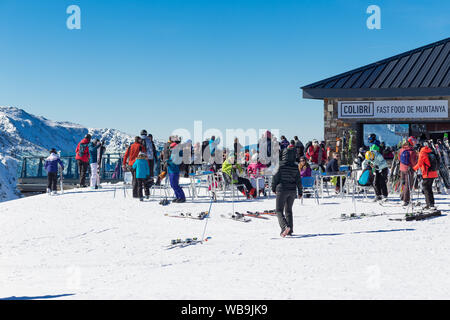 Pirenei, Andorra - 13 febbraio 2019: Sconosciuto turisti in una stazione sciistica in una caffetteria sul lato di una montagna. Inverno giornata di sole, sedie e tavoli superarvi Foto Stock