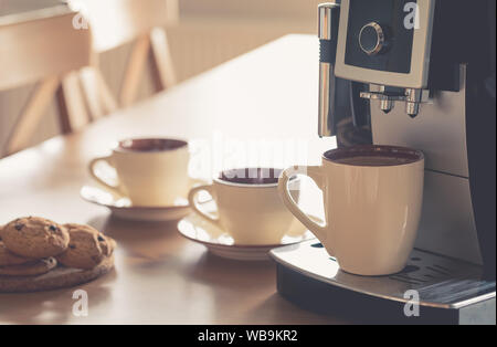 Tazze di caffè espresso mattutino nella macchina per caffè con biscotti sul tavolo di legno, tonica Foto Stock