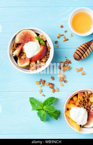 Muesli con figure, di pesche e yogurt in ciotola di legno blu sfondo tabella. Vista dall'alto. Concetto di mangiare sano, dieta e benessere Foto Stock