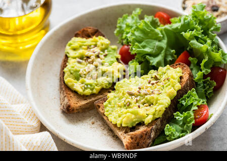 La colazione avocado toast con semi e insalata verde sulla piastra, primo piano Foto Stock