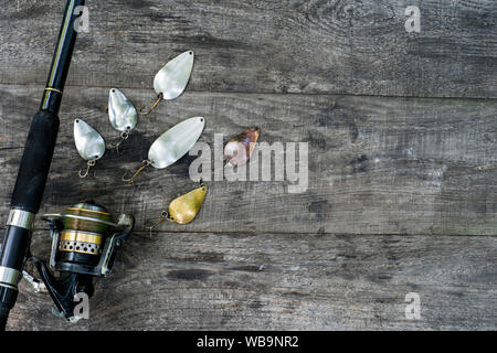 A forma di cucchiaio i filatori in vari colori con asta di filatura con bobina sull'annata sullo sfondo di legno. Il concetto della scelta di esca per diverse attività di pesca c Foto Stock