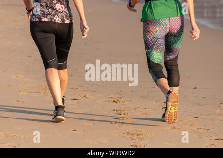 Una chiusura vista posteriore di due donne facendo loro corsa mattutina sulla spiaggia Foto Stock
