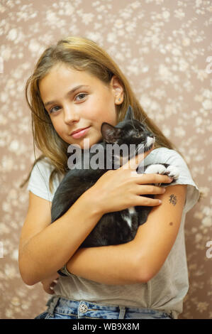 Ragazza di 10 anni e di un bianco e nero gattino. Bella bruna ragazza e gatto nero. Cute cat nelle braccia di un bambino. Ragazza a casa con il suo animale domestico. Accesa Foto Stock