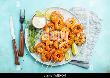 Spiedini o langostine di gamberi grigliati serviti con lime, aglio e salsa su fondo di cemento azzurro. Frutti di mare e birra. Vista dall'alto. Disposizione piatta Foto Stock