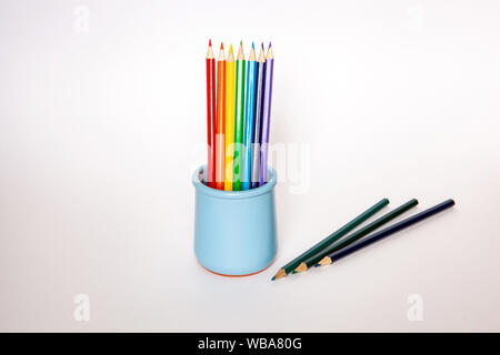 Set di matite colorate nel vaso blu su sfondo bianco. Foto Stock