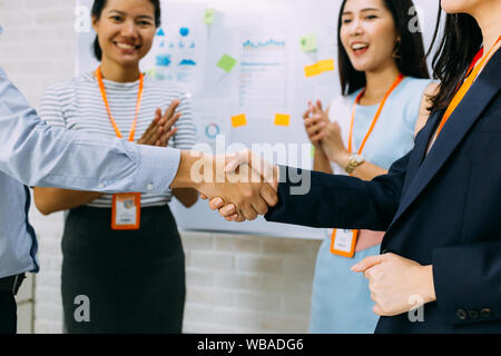 Giovani asiatici uomo d affari e business donna dando un gesto di handshake e rasserenanti lavoratori aziendali battendo le mani sullo sfondo della sala meeting Foto Stock