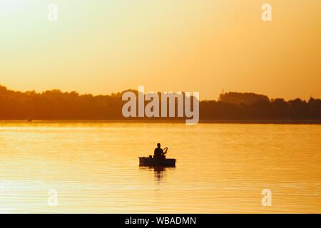 Silhouette di un pescatore che cattura il pesce in un bellissimo lago al tramonto Foto Stock